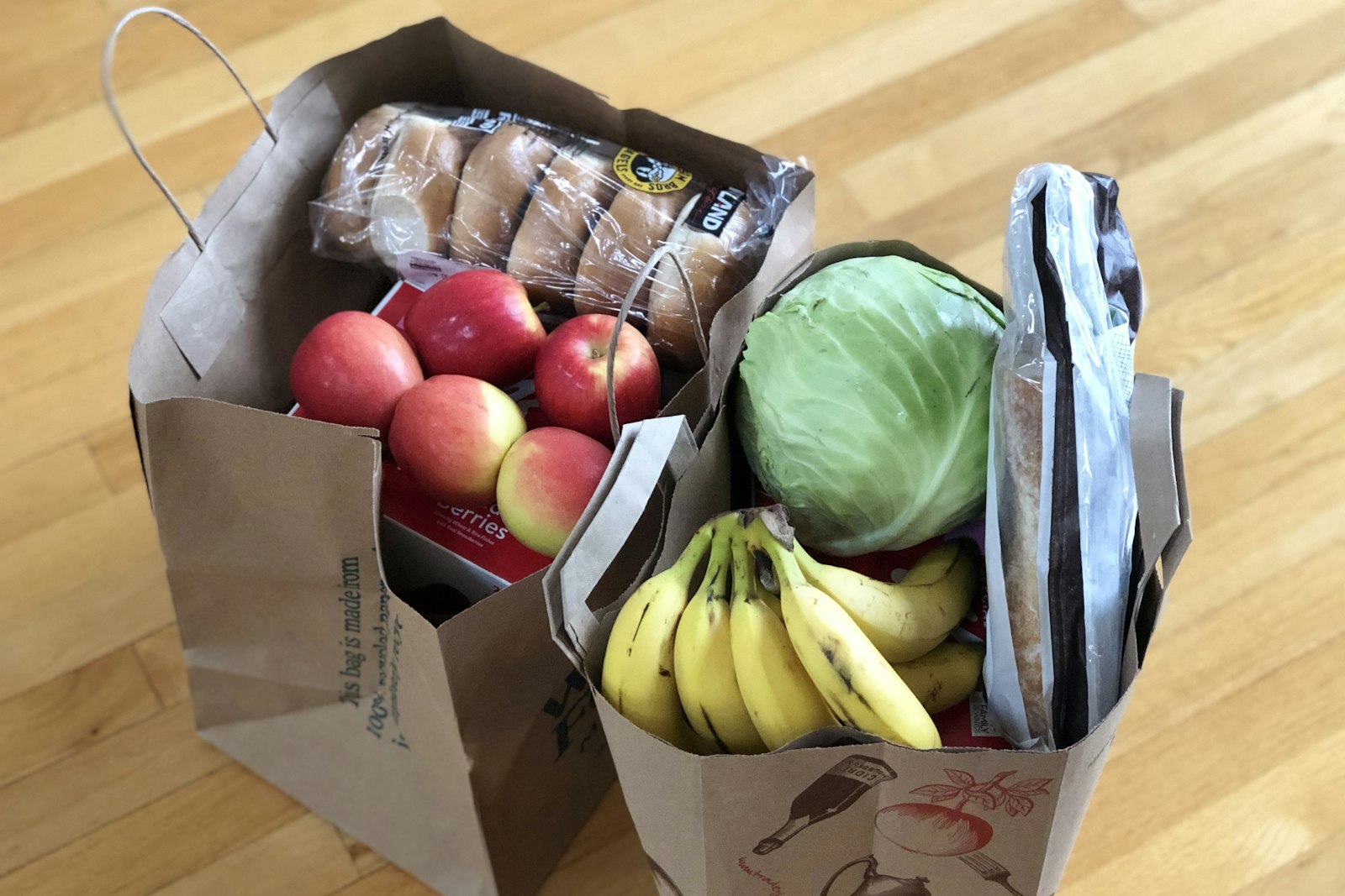 Paper grocery bags filled with apples, cabbage and bananas