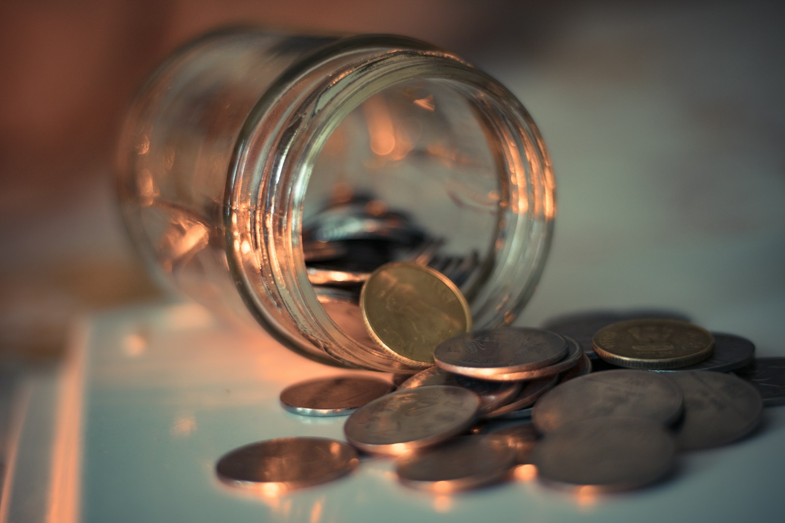 A glass jar tipped over with coins spilling out